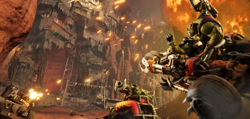 Screenshot aus Warhammer 40,000: Speed Freeks. Mehrere Orks liefern sich in bewaffneten Fahrzeugen ein rasantes Rennen durch eine zerstörte Wüstenlandschaft. Explosionen, Feuer und Geschosse sorgen für chaotische Action auf der Strecke.